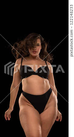 Overweight woman in black lingerie posing with, exuding self-confidence, elegance, and celebration of natural beauty against black studio background. Overweight woman in black lingerie posing with, exuding self-confidence, elegance, and celebration of natural beauty against black studio background. 122148233