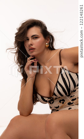 Portrait of charming, chubby young lady, dressed stylish clothes and accessories, sitting looking at camera with confidence against white studio background. 122148261