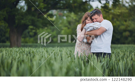 Loving parents cuddling newborn amid lush green meadow, sharing tender family connection Loving parents cuddling newborn amid lush green meadow, sharing tender family connection 122148290