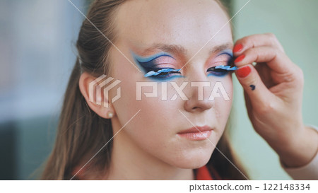 Professional makeup artist applying false eyelashes, creating dramatic eye makeup for fashion photoshoot Professional makeup artist applying false eyelashes, creating dramatic eye makeup for fashion photoshoot 122148334