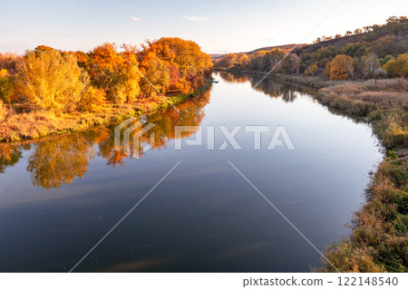 Multicolored autumn trees in the sun on the river bank. Autumn landscape. Bright colors of autumn by the river. Multicolored autumn trees in the sun on the river bank. Autumn landscape. Bright colors of autumn by the river. 122148540