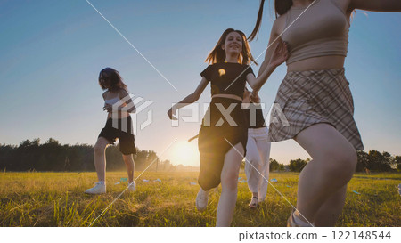 Four high school students enjoying a sunset run across a sunlit field, celebrating the freedom and thrill of summer break 122148544