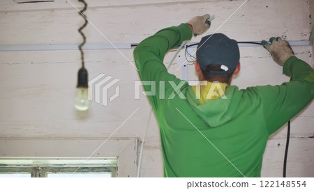 An electrician conducts wiring in a wooden house. 122148554