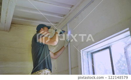 An electrician works with a drill to create electrical wiring. An electrician works with a drill to create electrical wiring. 122148579