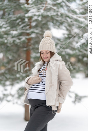 Young pregnant woman in a snowy winter forest, copy space. Expecting mother smiling and looking at her belly outdoors, natural light. Concept of maternity, love and joy of pregnancy. Young pregnant woman in a snowy winter forest, copy space. Expecting mother smiling and looking at her belly outdoors, natural light. Concept of maternity, love and joy of pregnancy. 122148945
