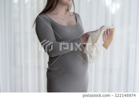Young pregnant woman getting ready for the maternity hospital preparing and planning baby clothes for new baby, packing for maternity hospital at home  Young pregnant woman getting ready for the maternity hospital preparing and planning baby clothes for new baby, packing for maternity hospital at home  122148974