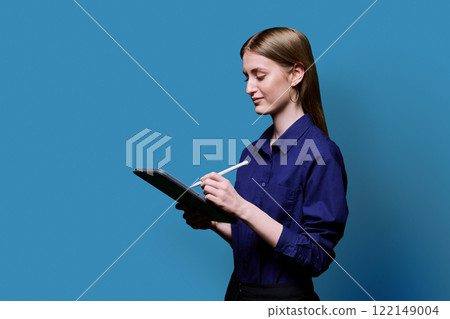 College student girl using digital tablet, profile view, blue background 122149004