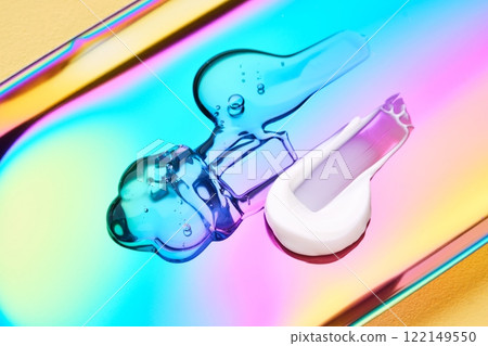 A drop of cosmetic serum, cream and gel on a multicolored background in shades of blue and lilac. A drop of cosmetic serum, cream and gel on a multicolored background in shades of blue and lilac. 122149550