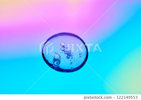 A drop of cosmetic serum on a multicolored background in shades of blue and lilac. A drop of cosmetic serum on a multicolored background in shades of blue and lilac. 122149553