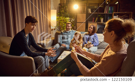 Teen boy talks to psychologist, discussing concerns, while his family listens attentively in the background. Maintaining productive communication Teen boy talks to psychologist, discussing concerns, while his family listens attentively in the background. Maintaining productive communication 122150109