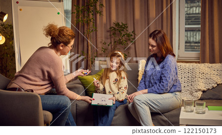 Mother with her child visiting psychologist for common psychological session. Girl drawing and presenting in to a female therapist. Maintaining positive communication 122150173