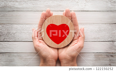 Hands Holding Wooden Heart Symbol of Love and Care on White Rustic Background 122150252