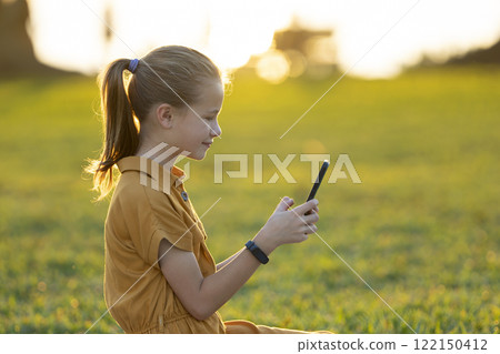 Happy teenage girl messaging on her cellphone outdoors sitting in summer park 122150412