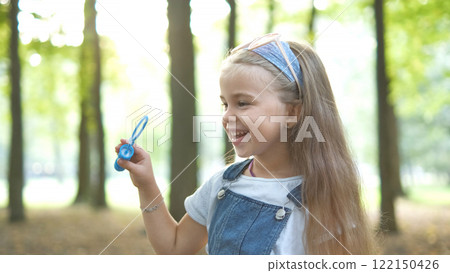 Happy little child girl blowing soap bubbles outside in green park. Outdoor summer activities for children concept. Happy little child girl blowing soap bubbles outside in green park. Outdoor summer activities for children concept. 122150426