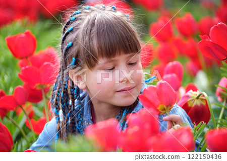 Happy child girl playing in summer garden enjoying sweet scent of red tulip flowers on sunny day 122150436