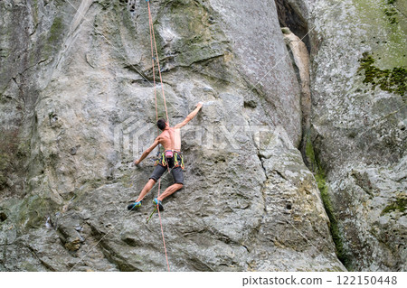 Determined climber clambering up steep wall of rocky mountain. Sportsman overcoming difficult route. Engaging in extreme sports and rock climbing hobby concept. Determined climber clambering up steep wall of rocky mountain. Sportsman overcoming difficult route. Engaging in extreme sports and rock climbing hobby concept. 122150448