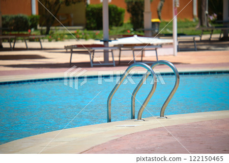 Close up of swimming pool stainless steel handrail descending into tortoise clear pool water. Accessibility of recreational activities concept. 122150465