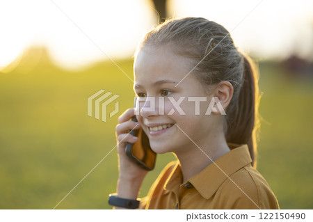 Child girl talking with her friend on cellphone outdoors in summer park Child girl talking with her friend on cellphone outdoors in summer park 122150490