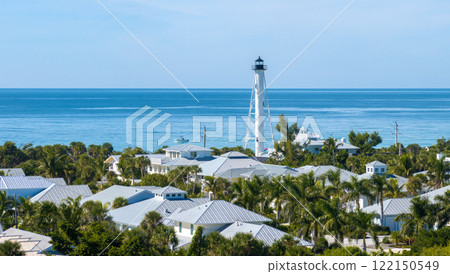 Boca Grande, Florida architecture. White lighthouse tower and wealthy neighborhood with expensive waterfront houses between green palm trees. Development of US premium housing Boca Grande, Florida architecture. White lighthouse tower and wealthy neighborhood with expensive waterfront houses between green palm trees. Development of US premium housing 122150549