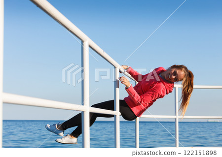 Woman fool around sitting on handrail near sea Woman fool around sitting on handrail near sea 122151898