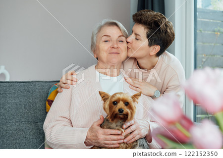 Neutral gender woman kissing her senior mom or grandma, sharing a tender moment together. Parenting love, care and generations unity concept. Mothers day. Happy family enjoying weekend together Neutral gender woman kissing her senior mom or grandma, sharing a tender moment together. Parenting love, care and generations unity concept. Mothers day. Happy family enjoying weekend together 122152350