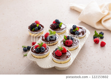 Mini vanilla cheesecakes cooked in a muffin pan with chocolate ganache served with fresh berries 122153602