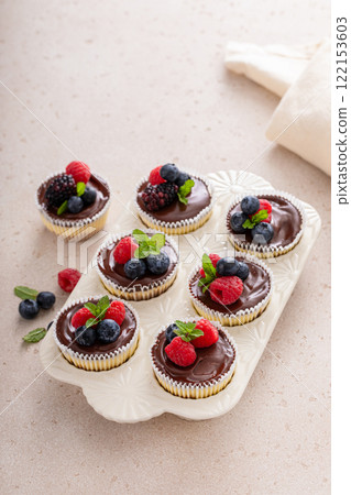 Mini vanilla cheesecakes cooked in a muffin pan with chocolate ganache served with fresh berries 122153603