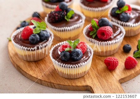 Mini vanilla cheesecakes cooked in a muffin pan with chocolate ganache served with fresh berries Mini vanilla cheesecakes cooked in a muffin pan with chocolate ganache served with fresh berries 122153607