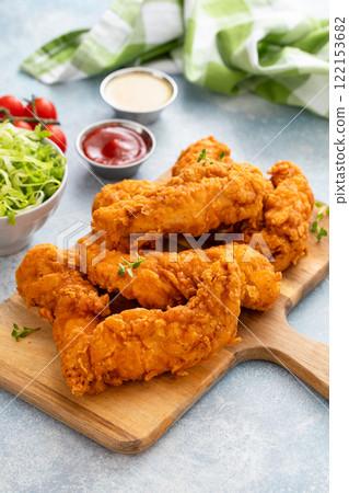 Fried chicken tenders on a serving board with sauces and salad Fried chicken tenders on a serving board with sauces and salad 122153682