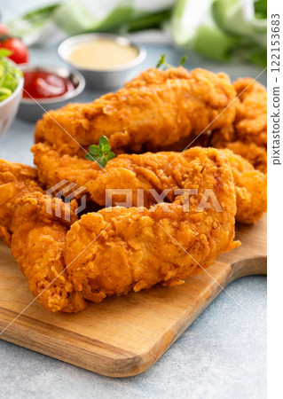 Fried chicken tenders on a serving board with sauces and salad Fried chicken tenders on a serving board with sauces and salad 122153683