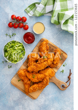 Fried chicken tenders on a serving board with sauces and salad Fried chicken tenders on a serving board with sauces and salad 122153685