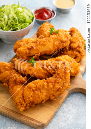 Fried chicken tenders on a serving board with sauces and salad Fried chicken tenders on a serving board with sauces and salad 122153689