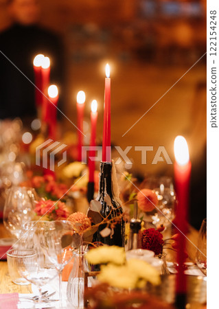 Elegant candlelit dinner table with red candles, floral arrangements, and a cozy ambiance 122154248