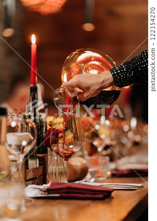 Decanting red wine into a glass on a festive dinner table with elegant decor and candlelight 122154270