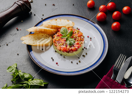 Guacamole tartare with fresh vegetables, basil garnish, and crispy baguette slices on a white plate 122154273