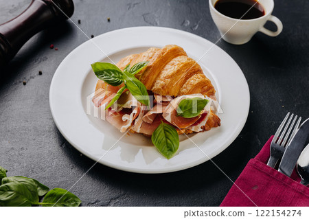 Fresh croissant sandwich with prosciutto and basil served on plate, perfect for a gourmet breakfast Fresh croissant sandwich with prosciutto and basil served on plate, perfect for a gourmet breakfast 122154274