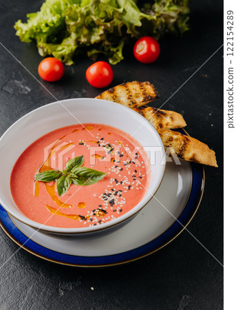 Fresh tomato soup with sesame seeds, basil garnish, and toasted bread for a comforting meal Fresh tomato soup with sesame seeds, basil garnish, and toasted bread for a comforting meal 122154289
