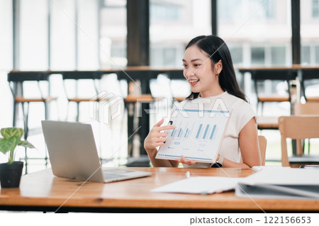 Professional woman showcasing data charts on a tablet in a bright, modern office environment. 122156653