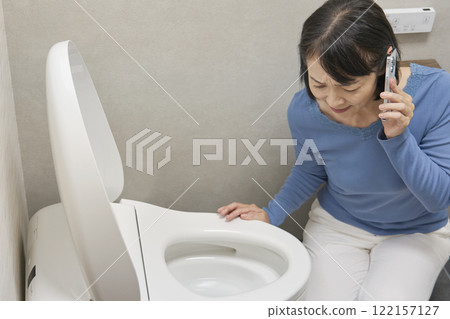 A woman calling a repairman in the bathroom A woman calling a repairman in the bathroom 122157127