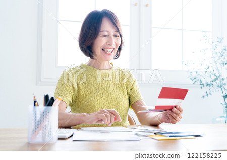A middle-aged woman preparing her tax return while looking at her bankbook A middle-aged woman preparing her tax return while looking at her bankbook 122158225