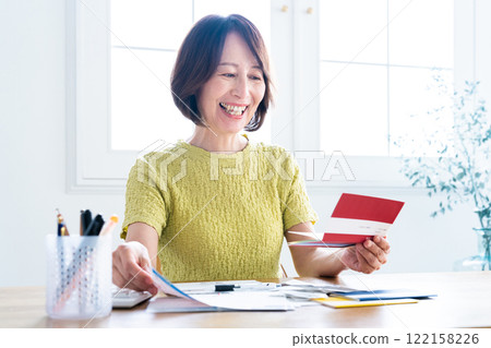 A middle-aged woman preparing her tax return while looking at her bankbook A middle-aged woman preparing her tax return while looking at her bankbook 122158226