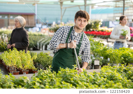 Guy employee of garden center is busy working with plants, potted Spearmint 122158420