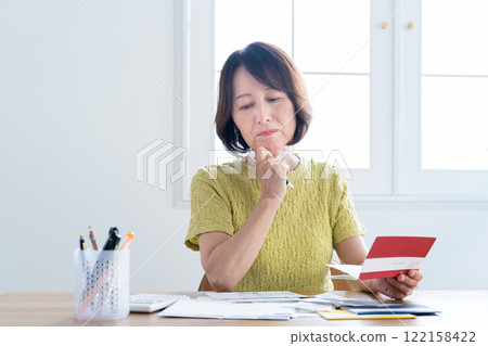 A middle-aged woman preparing her tax return while looking at her bankbook A middle-aged woman preparing her tax return while looking at her bankbook 122158422