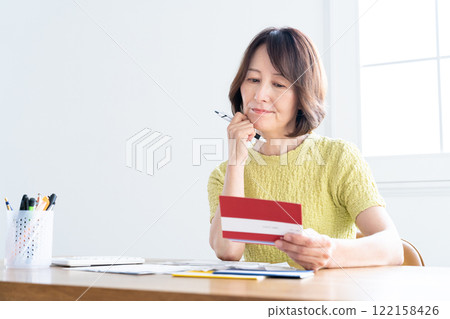 A middle-aged woman preparing her tax return while looking at her bankbook A middle-aged woman preparing her tax return while looking at her bankbook 122158426