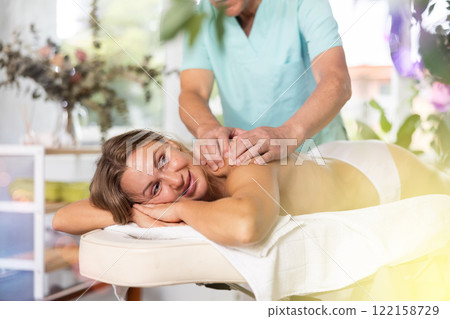 Relaxed middle-aged woman having back massage therapy conducted by skilled masseur Relaxed middle-aged woman having back massage therapy conducted by skilled masseur 122158729