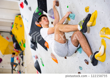 Young man grabbing ledges of artificial climbing wall Young man grabbing ledges of artificial climbing wall 122158735
