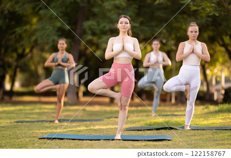 Group of young women doing yoga in tree pose 122158767