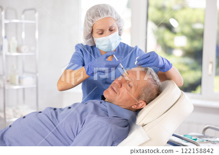 Doctor performs procedure of injectable correction of wrinkles in nasal bridge area for man 122158842