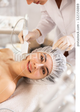Young female patient undergoing facial skin cleansing with ultrasonic shovel 122158869