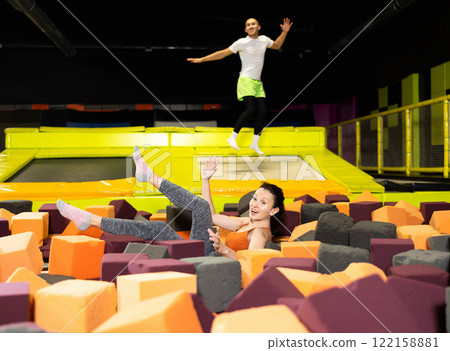 Fitness, fun, leisure and sport activity concept - happy woman fell on soft, safe filler cubes after jumping on trampoline Fitness, fun, leisure and sport activity concept - happy woman fell on soft, safe filler cubes after jumping on trampoline 122158881
